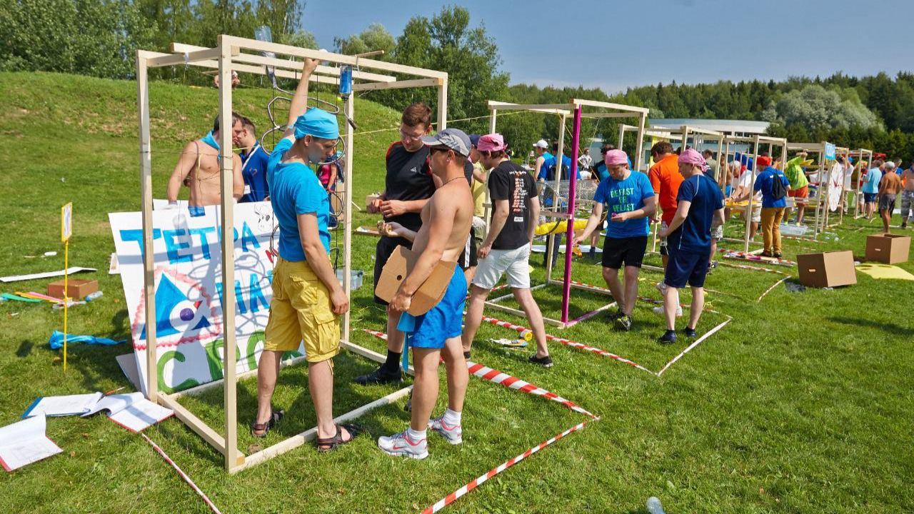 Participants of the summer team-building quest (team building) perform a physical task using wooden structures on a green lawn. Outdoor activities.