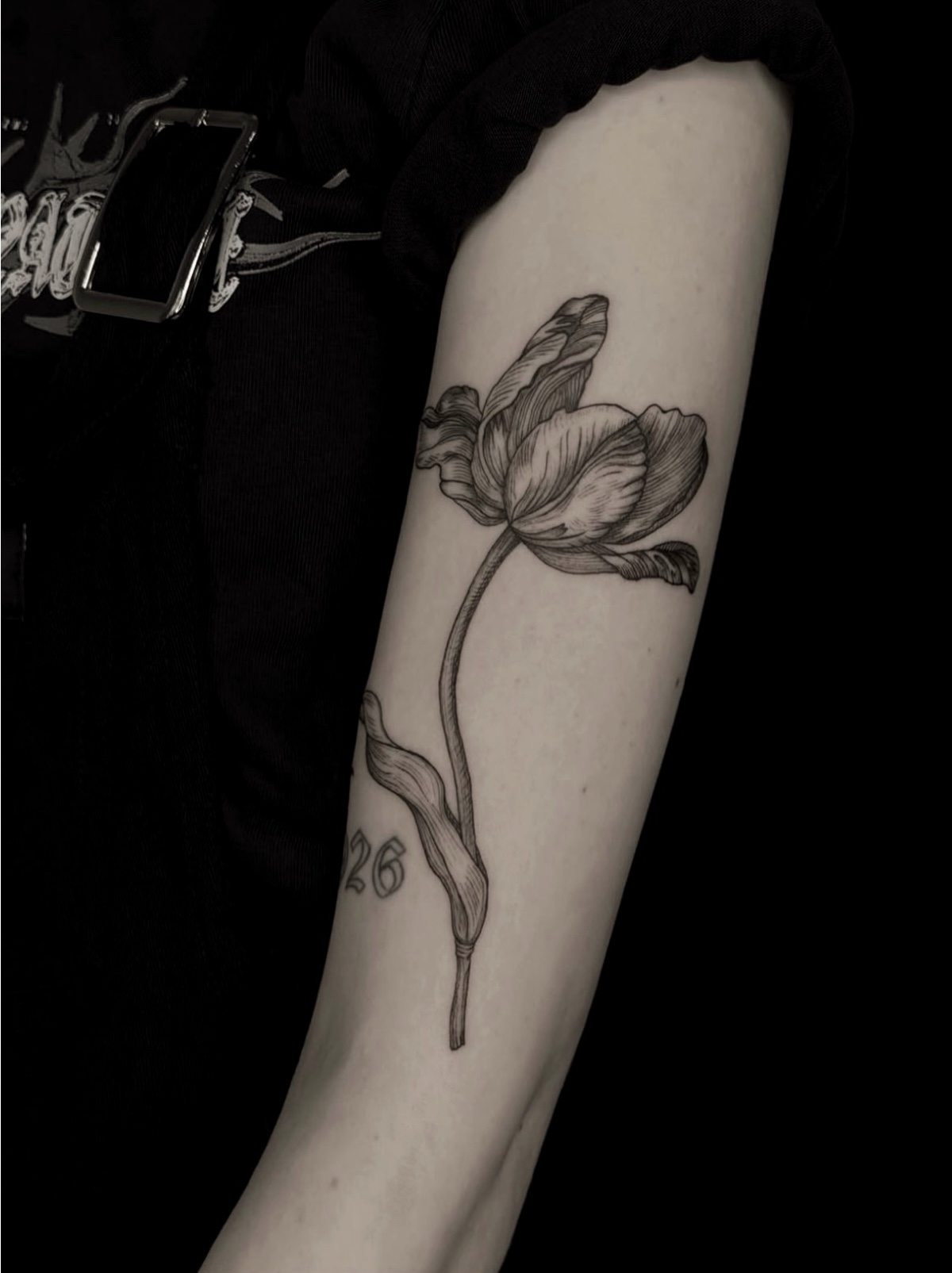 Arm tattoo of an open flower with wavy petals, a long curved stem and one folded leaf.