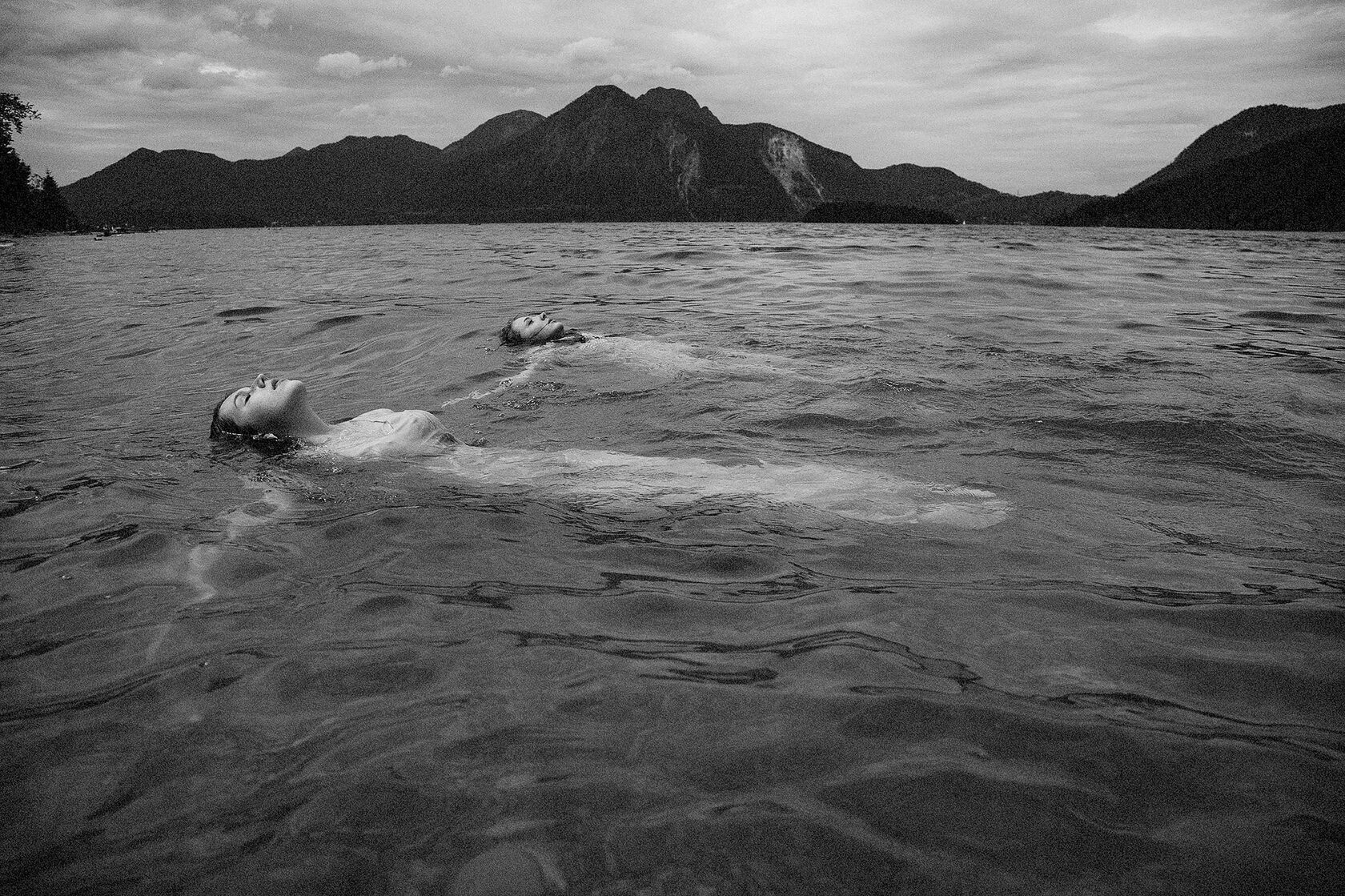 Schwarz-Weiß-Fotografie zweier Frauen auf dem Wasser vor einer Berglandschaft