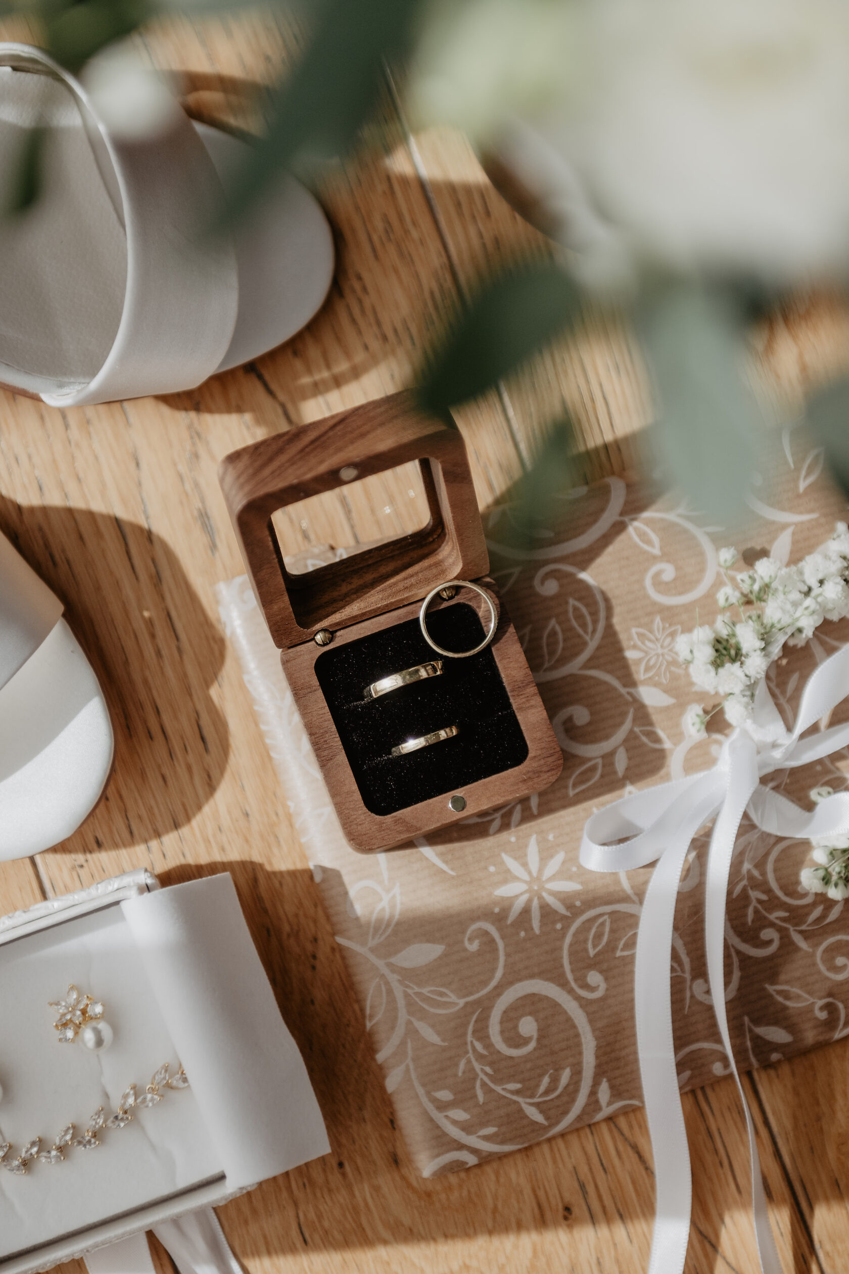 Wedding rings in a wooden ring box on wrapped gifts with ribbon, styled flat lay detail