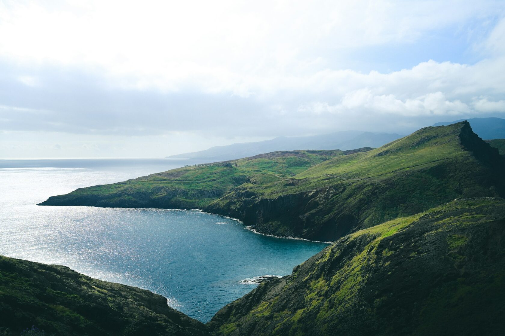 A narrow levada path winding along a steep green mountainside in Madeira, the ocean far below