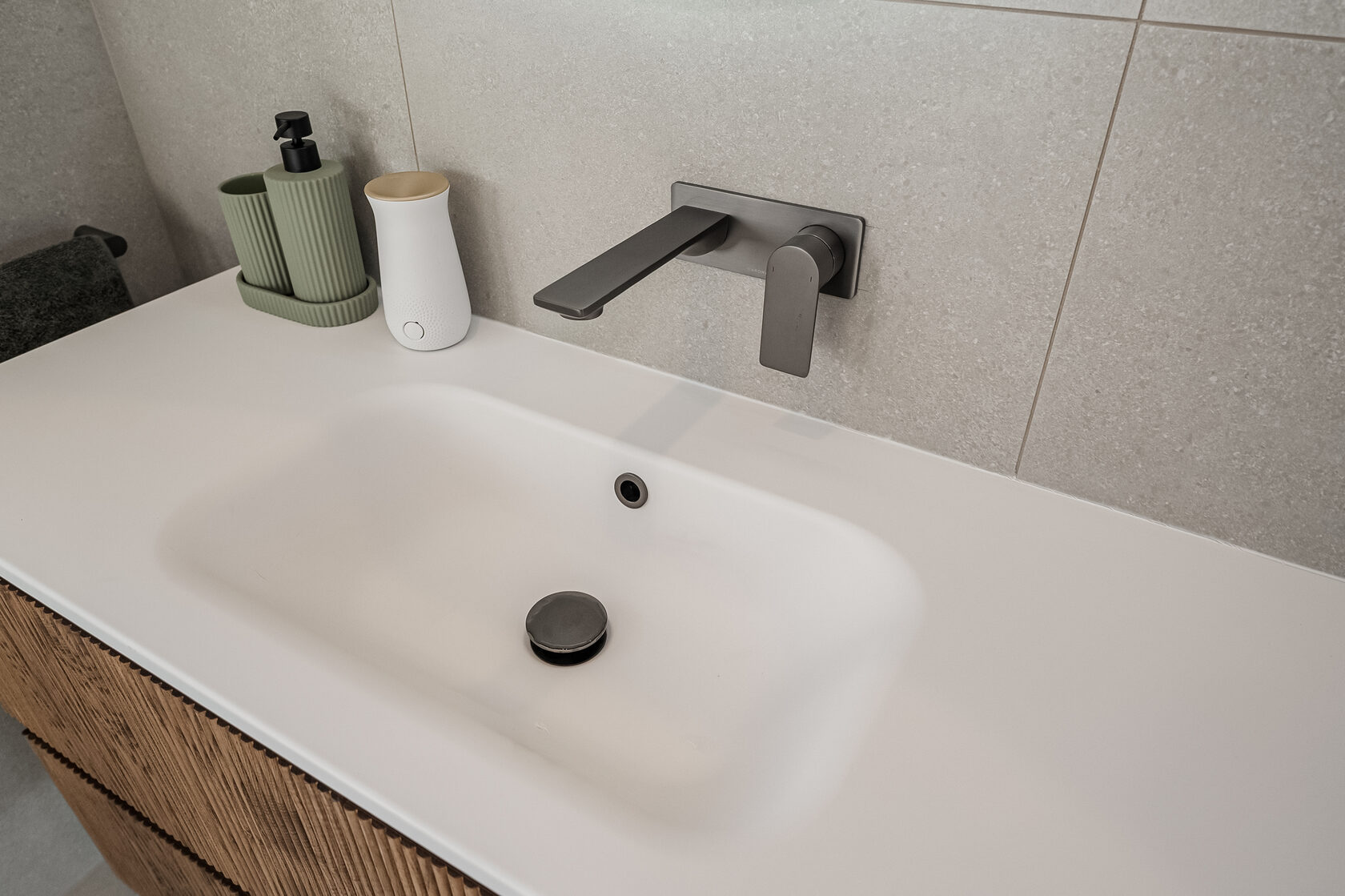 White bathroom basin with a wall-mounted dark tap against large grey tiles