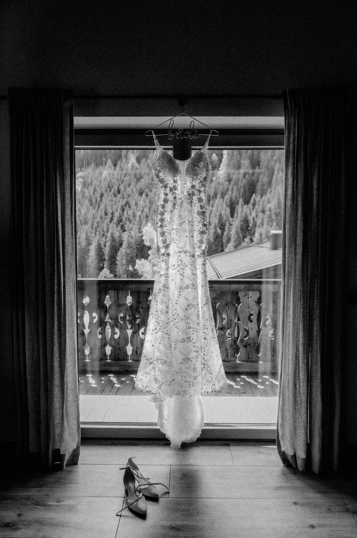 Wedding dress hanging in front of a window with forest view, black-and-white detail photo