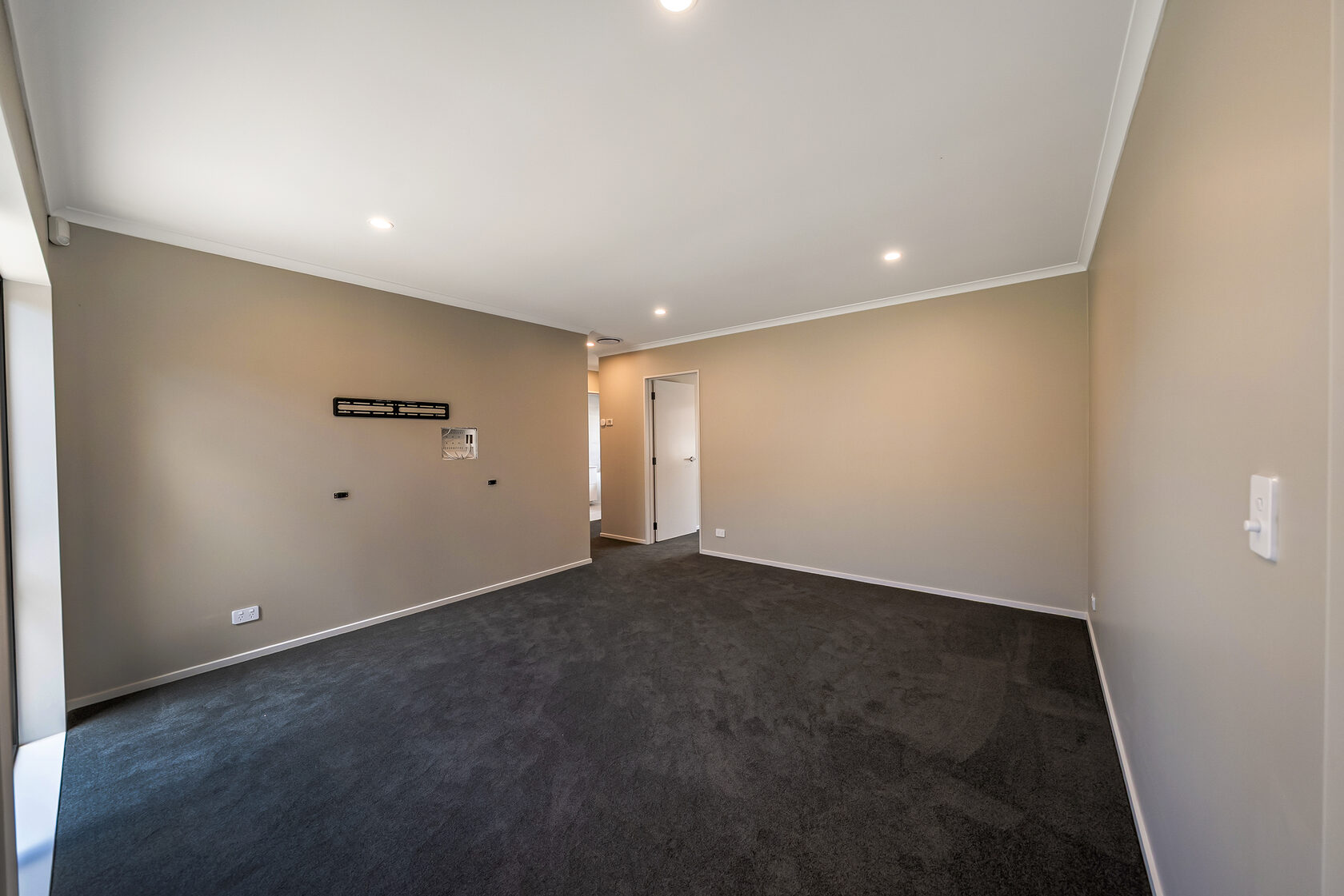 Empty carpeted room with neutral walls, recessed ceiling lights, and doorway leading to an adjoining space.