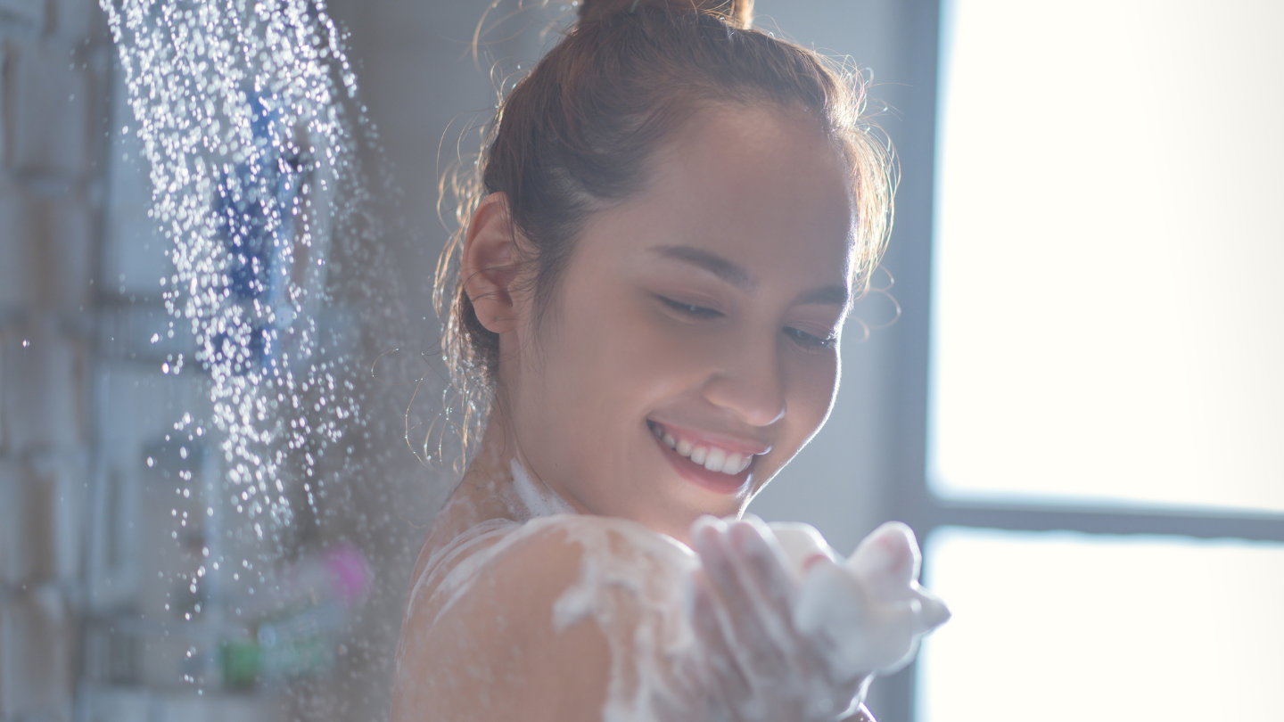 The image shows a smiling woman enjoying a shower with soft water, illustrating the benefits of water softeners for healthier skin and better lather formation