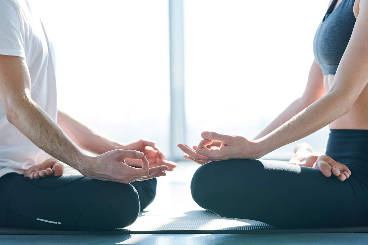 Un hombre y una mujer sentados con las piernas cruzadas sobre tapetes de yoga en una sala serena