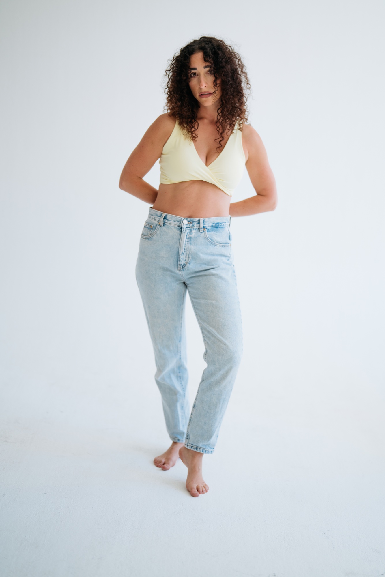 Ganzkörperaufnahme eines Models in hellem Top und blauer Jeans, barfuß im Studio
