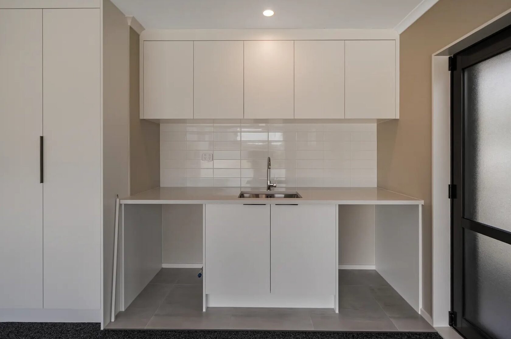 Renovated laundry with white cabinets, stainless steel sink, tiled splashback and appliance spaces