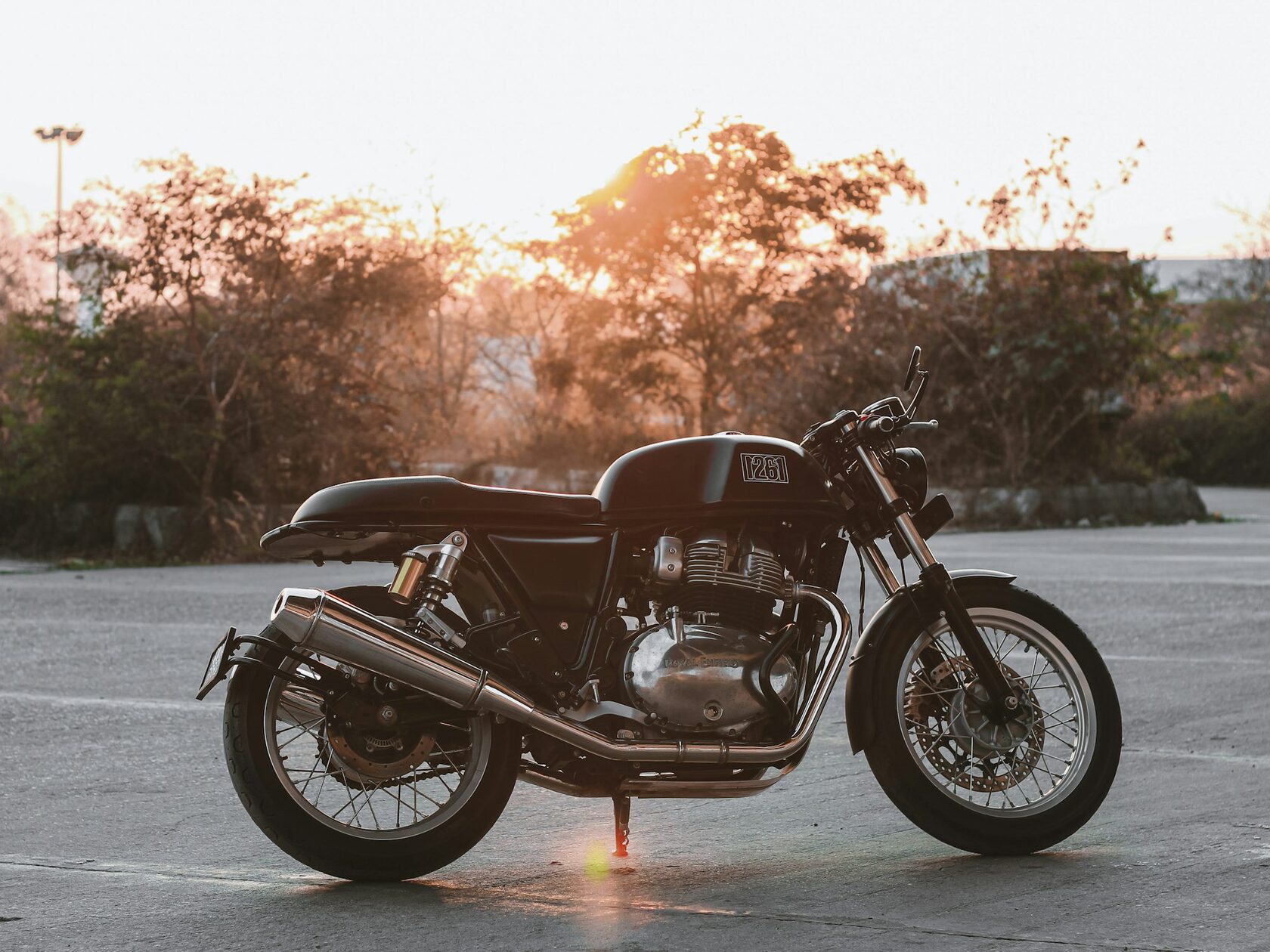 Royal Enfield Bear 650 scrambler motorcycle, front three‑quarter view, parked on a coastal road at golden hour