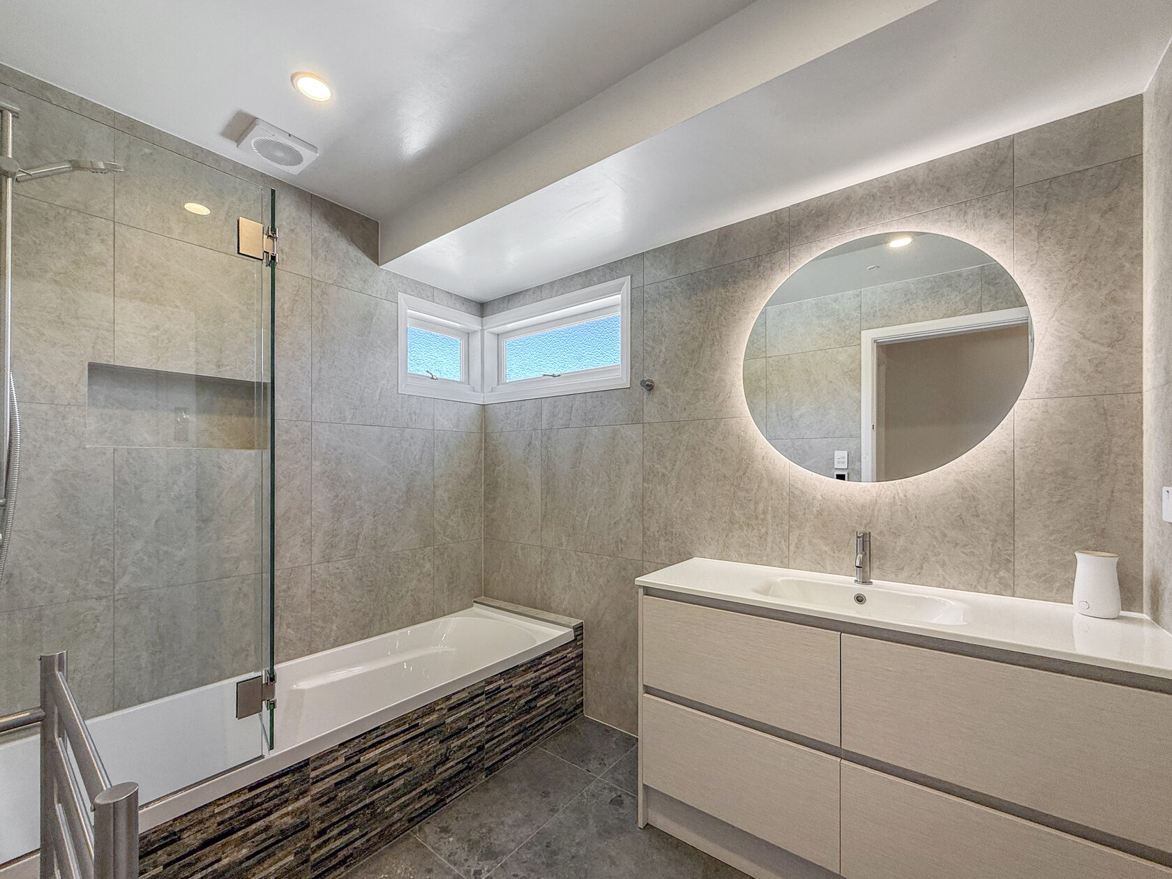 Renovated bathroom with a shower over the bath and an illuminated round mirror