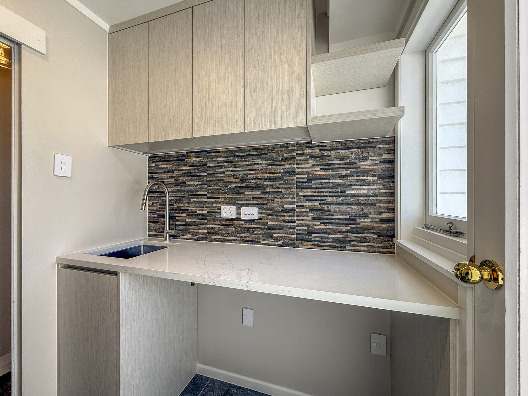 Utility room with white cabinets, sink and patterned stone-look splashback