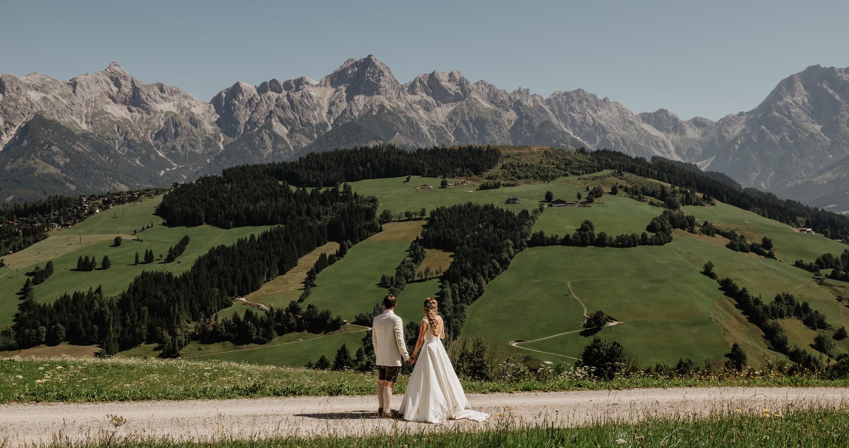 Wedding couple holding hands in a mountain valley with panoramic peaks and green hills behind