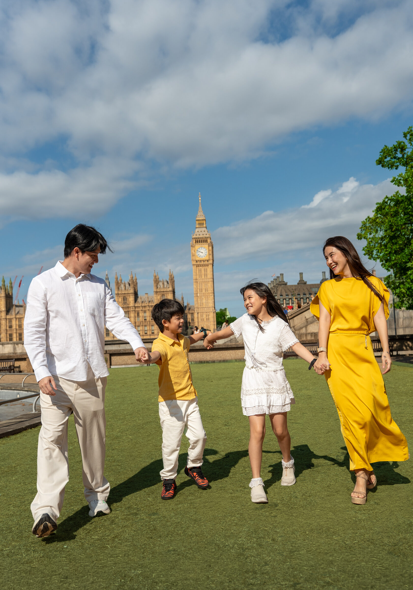 Family of four laughing and walking hand in hand in front of Big Ben
