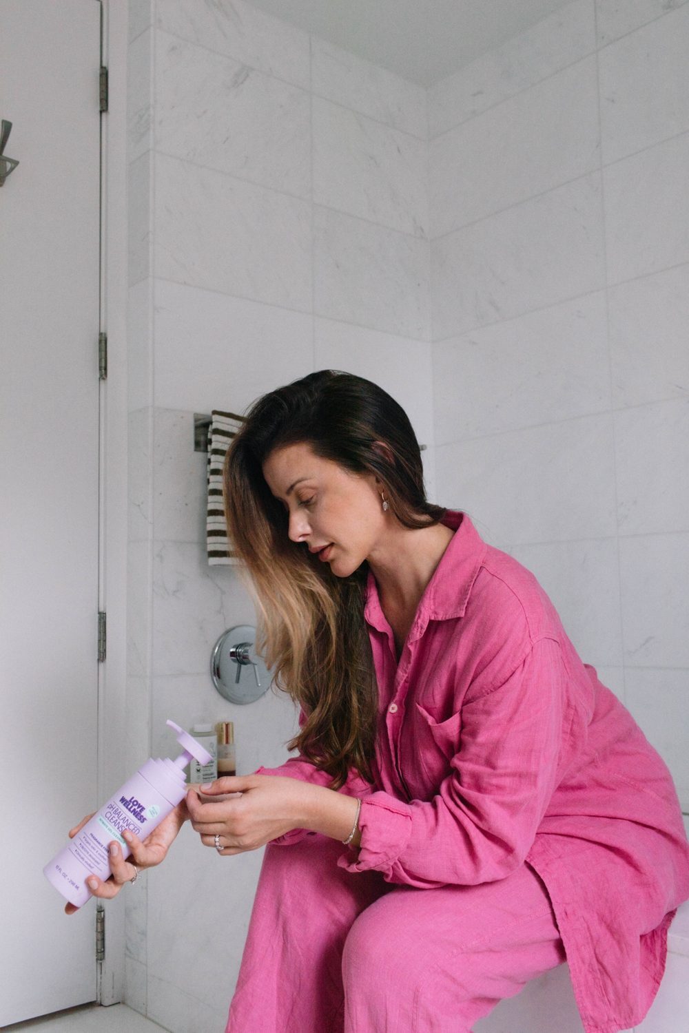 Lo in her bathroom reading a bottle of pH Balanced Cleanser