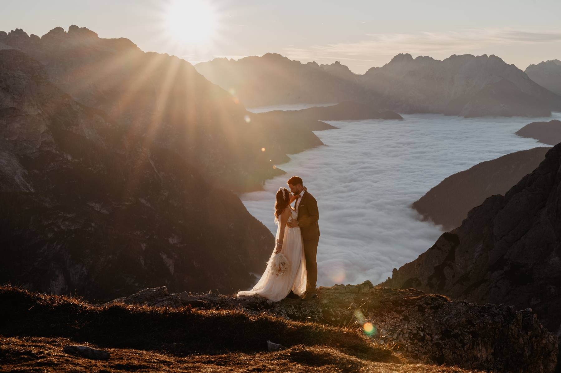 Bride and groom kissing at sunrise above a sea of clouds in the Dolomites, Italy, mountain elopement portrait
