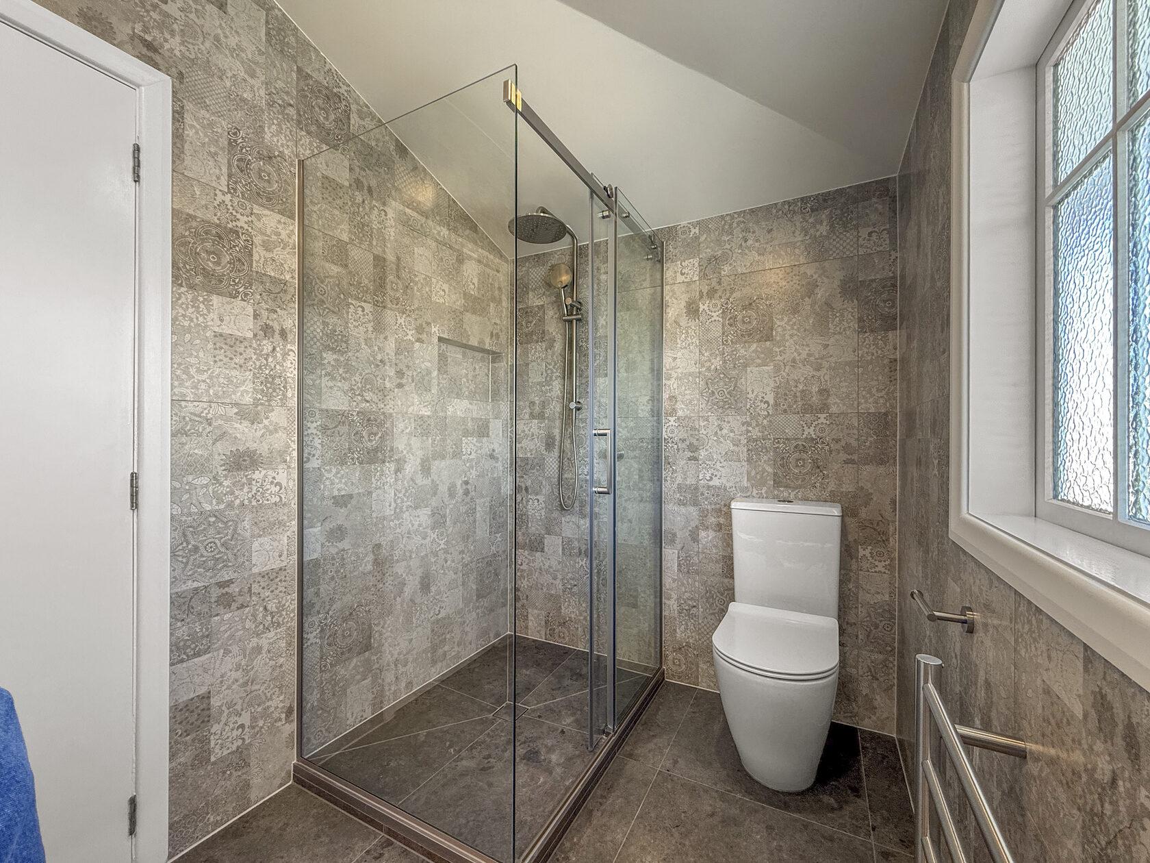 Glass shower enclosure and white toilet against patterned grey tiles
