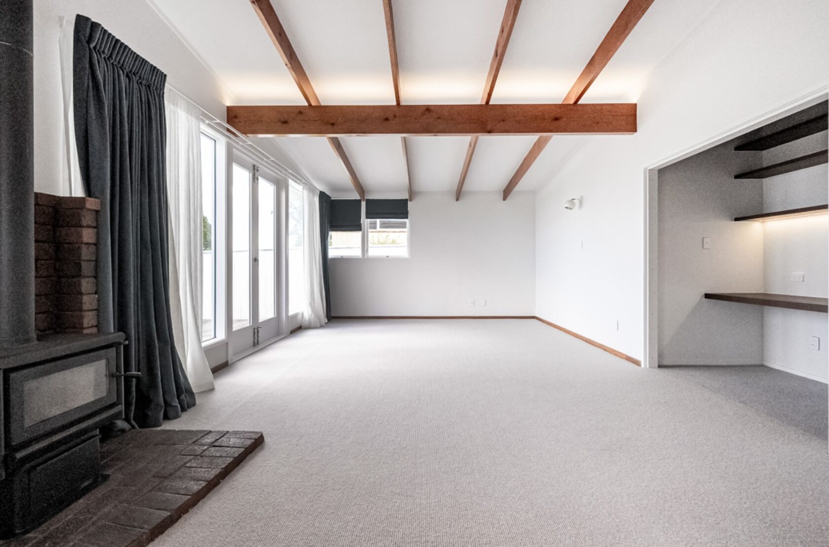 After: spacious Hillcrest living area with exposed beams, pale carpet and built-in desk