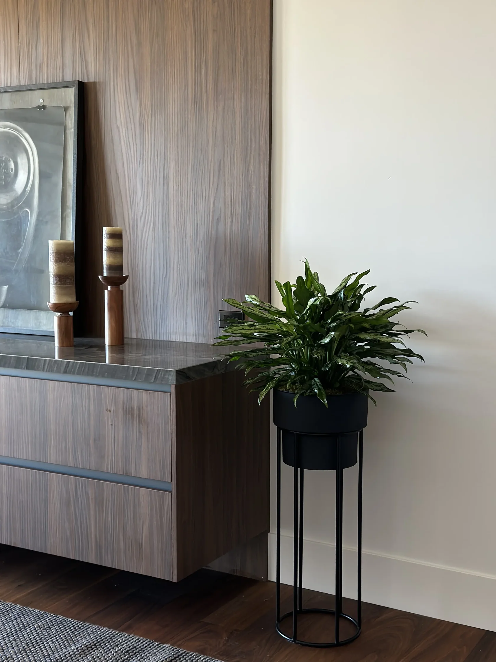 Peace lily on a black wire plant stand beside a wooden dresser