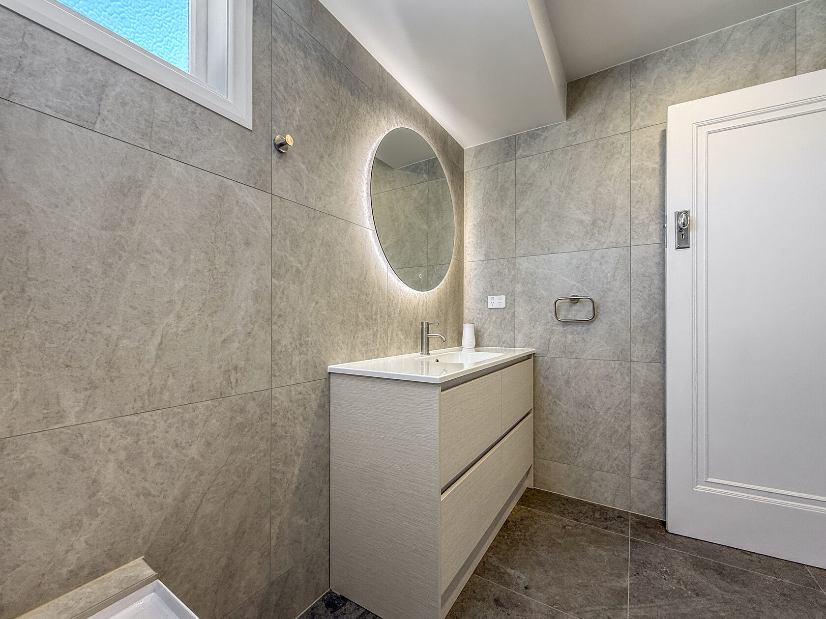 Bathroom vanity with mirror, pale cabinetry and tiled wall