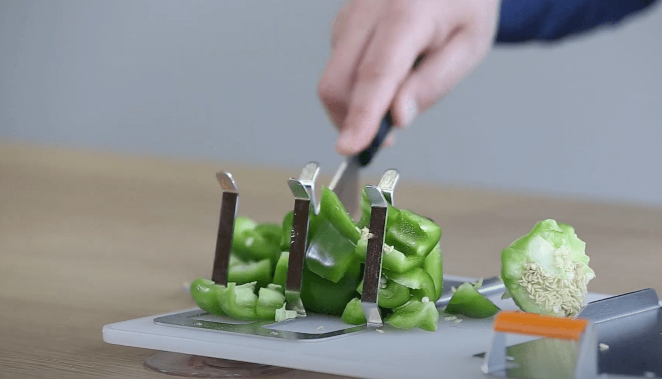 Cortar pimientos en cubos usando abrazaderas ajustables en una tabla de cortar adaptativa.