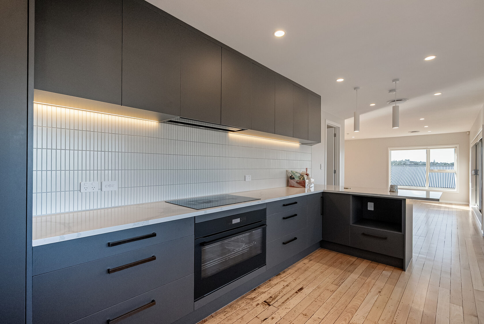 Open-plan Glenfield kitchen with dark cabinetry and pale benchtops opening into the bright family living area