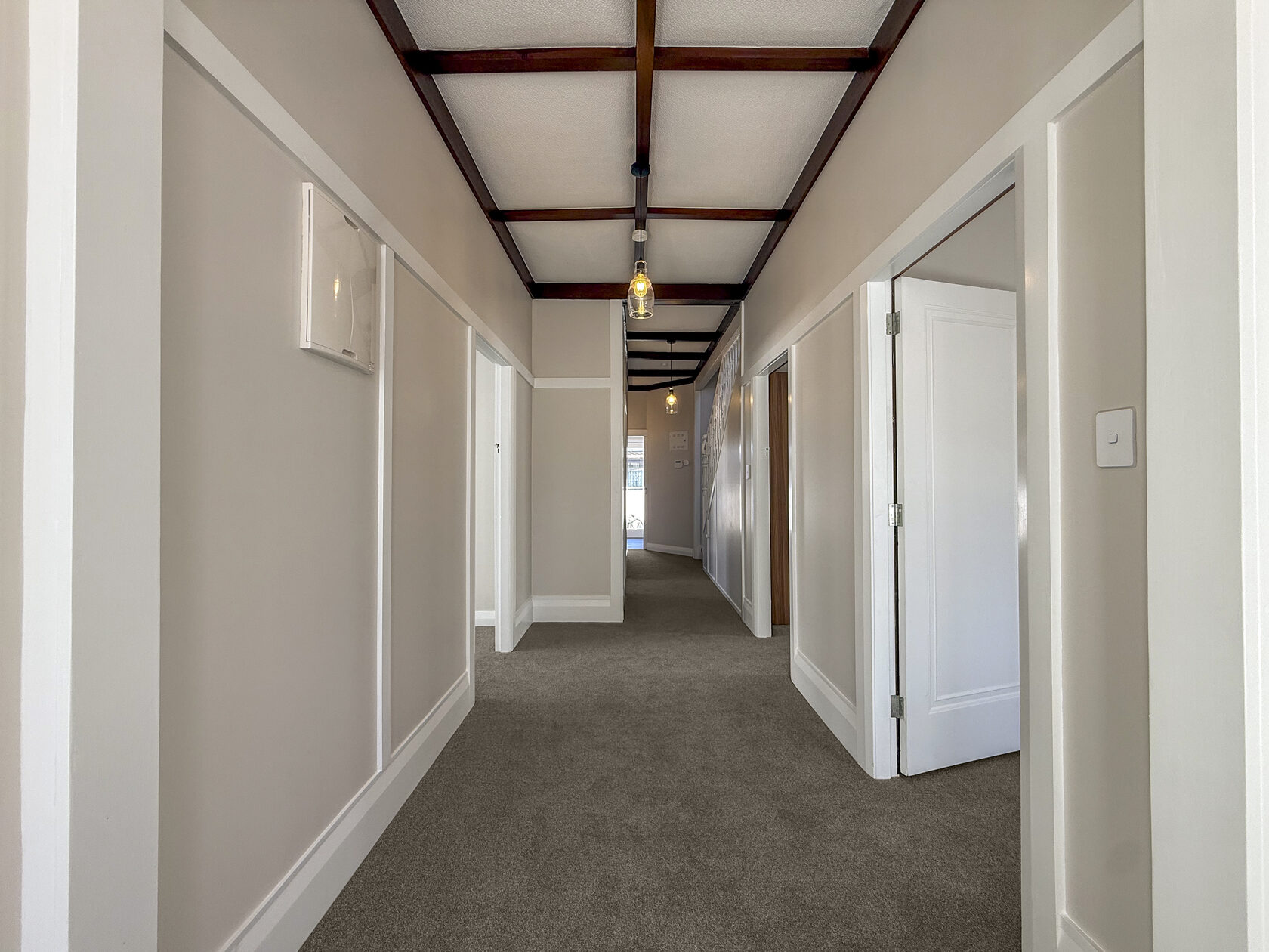Long carpeted hallway with exposed dark timber ceiling beams and white doors