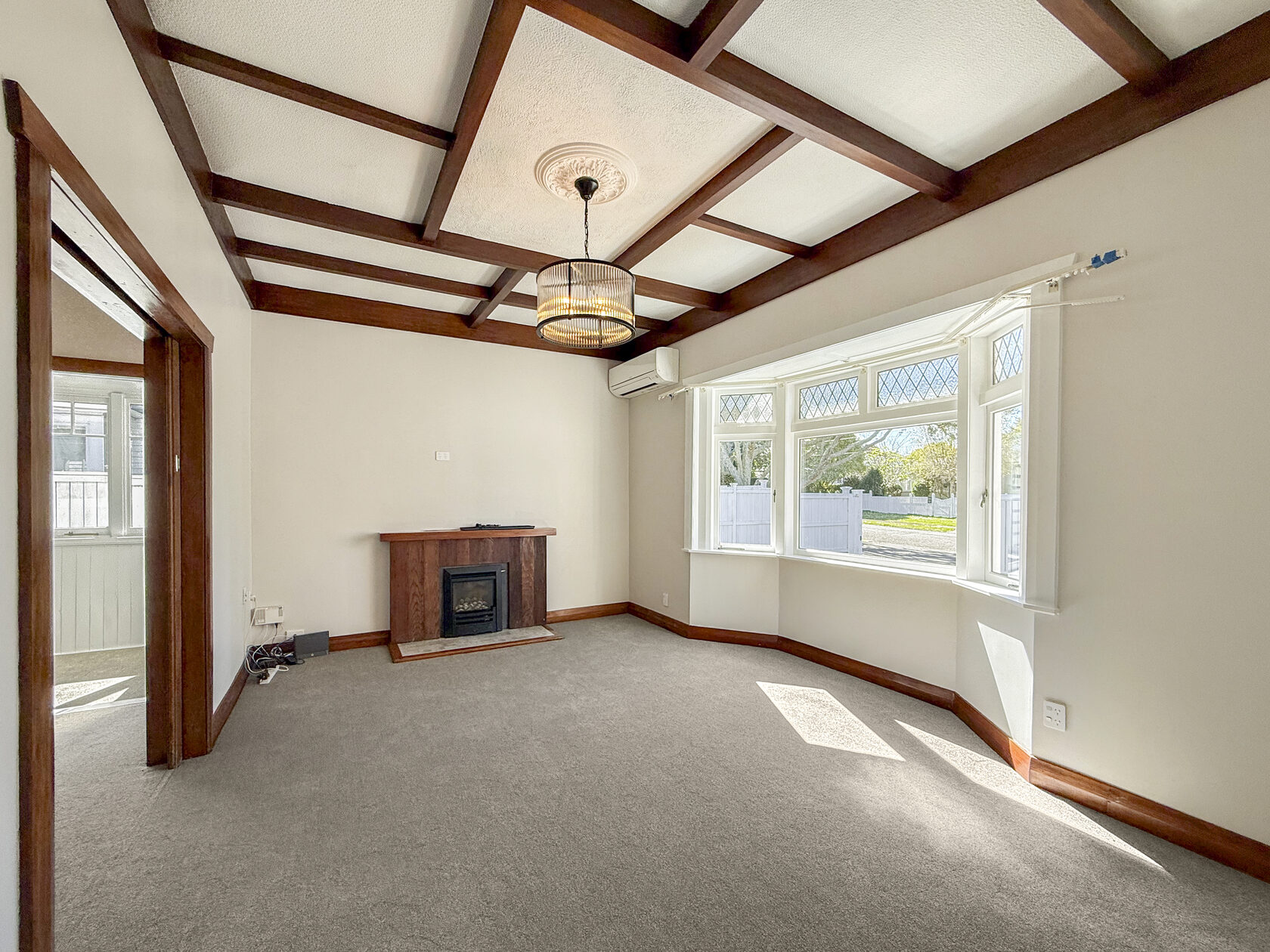 Another view of the carpeted living room with timber beams, fireplace and bay window