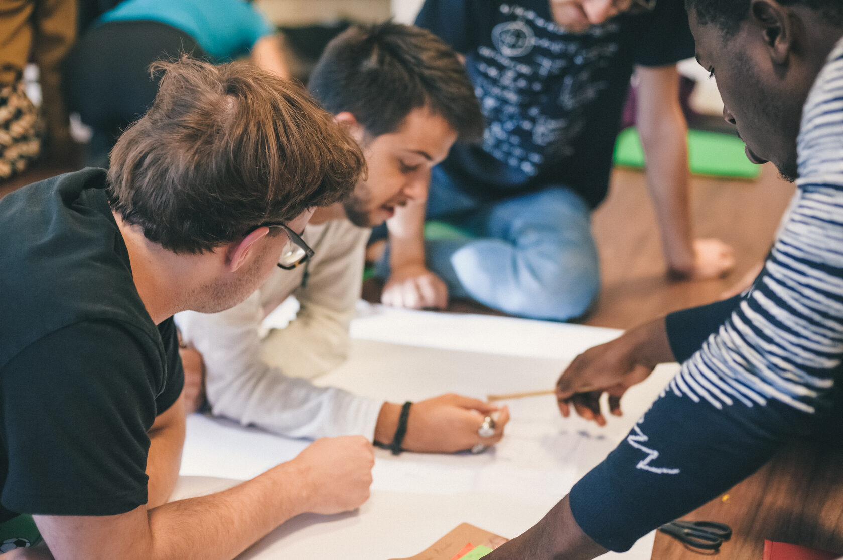Participants leaning over a table during a CWM workshop, writing and discussing together on a large sheet of paper.