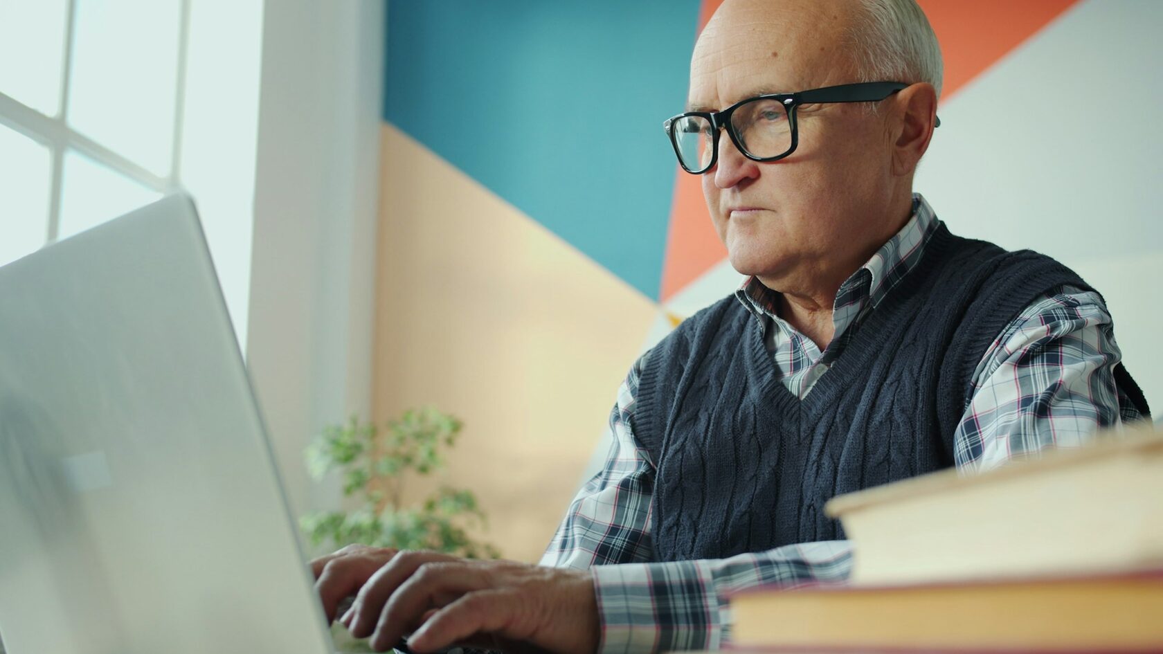 Osoba starsza siedząca przy komputerze i notująca podczas zapisu na program