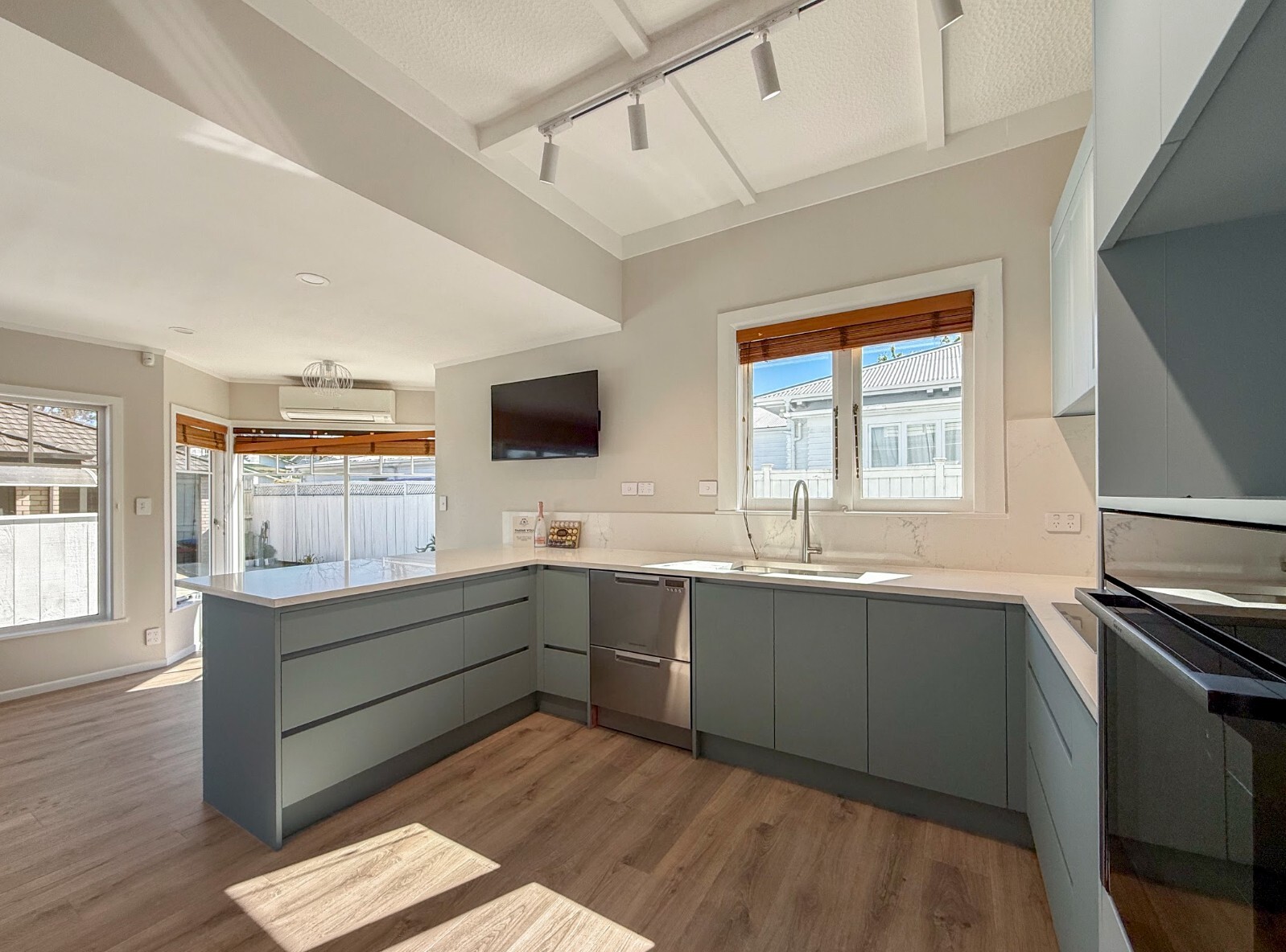 After renovation: kitchen with muted green cabinetry, white benchtops and timber-look flooring