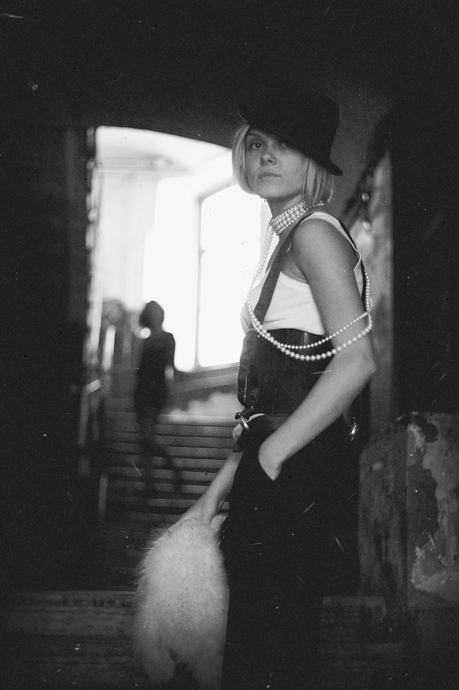 Schwarz-Weiß-Portrait einer Frau mit Hut und Perlenketten in einem Treppenhaus