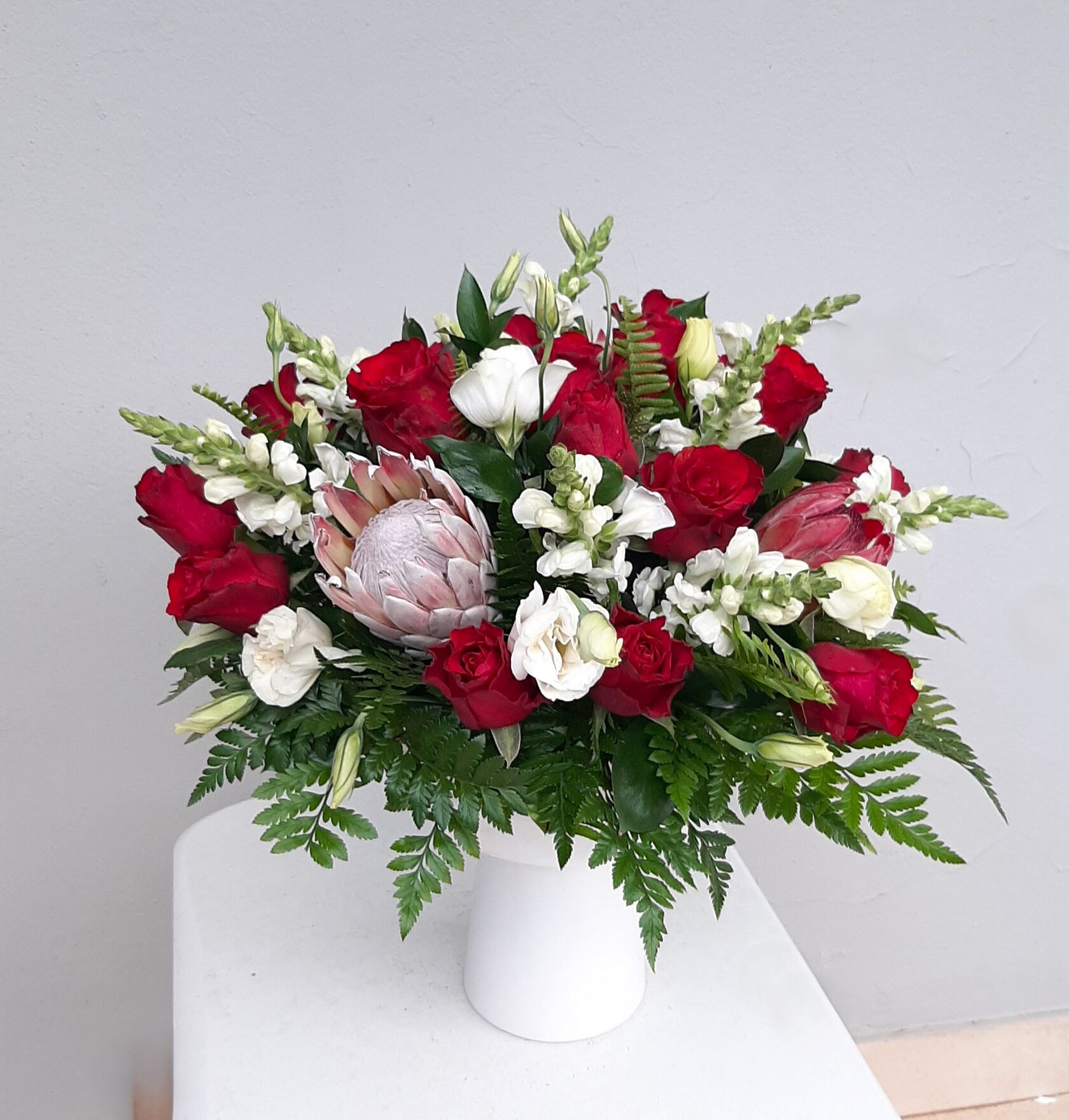 Floral arrangement with red roses and proteas.
