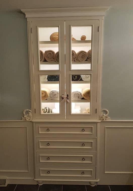 Bathroom built-in storage cabinet with lower drawers and decorative carved floral motif and lighted shelves