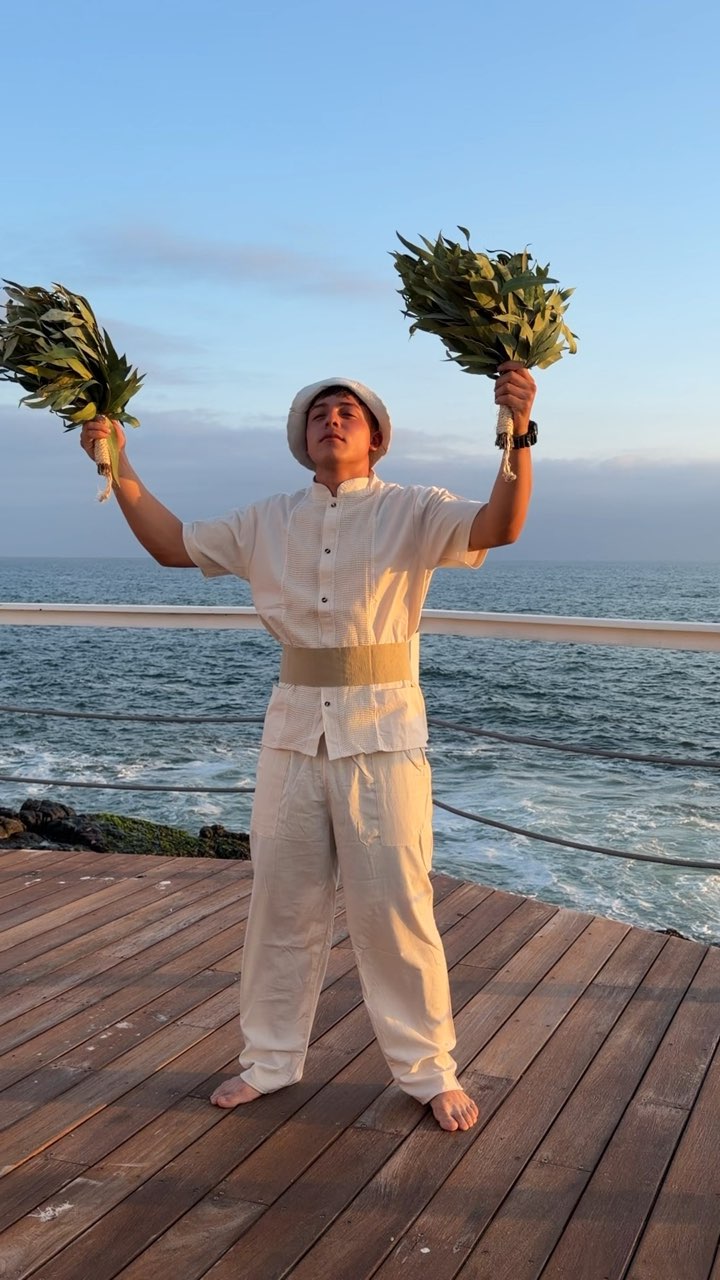 Una invitada levanta las ramas del venik frente al mar, bajo el cielo azul