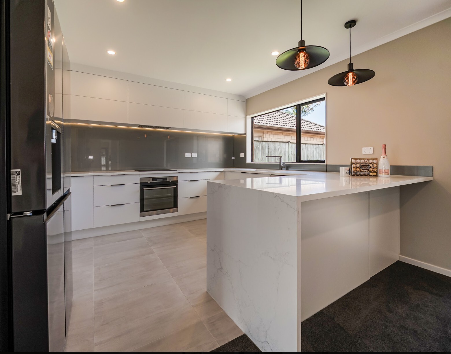 Renovated Flat Bush kitchen with white cabinetry, grey splashback, black refrigerator and peninsula beneath pendant lights