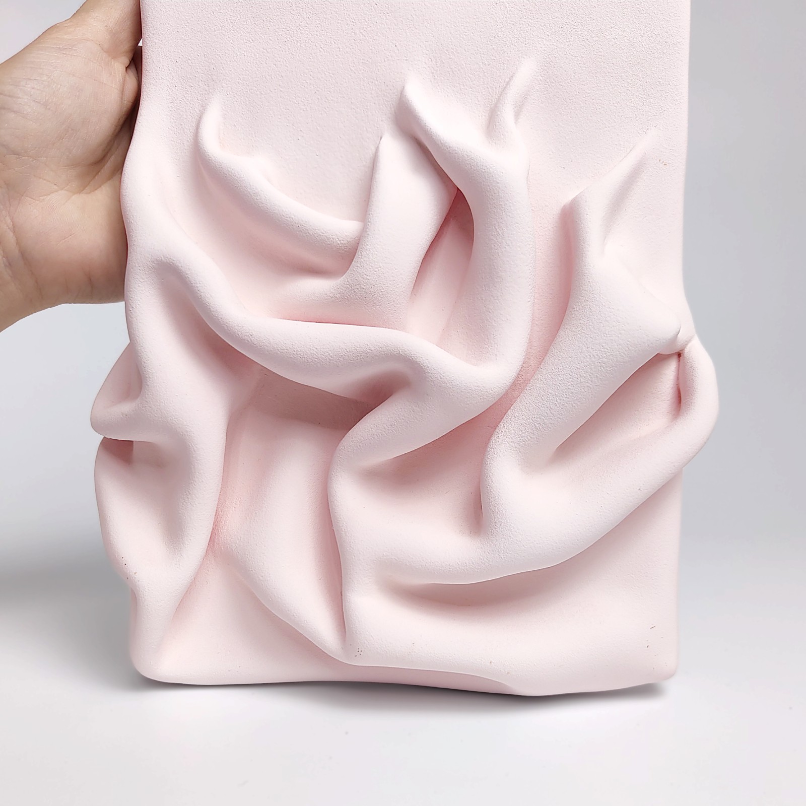 textured wall art made of air-dry clay in a soft pink shade with flowing sculpted drapery