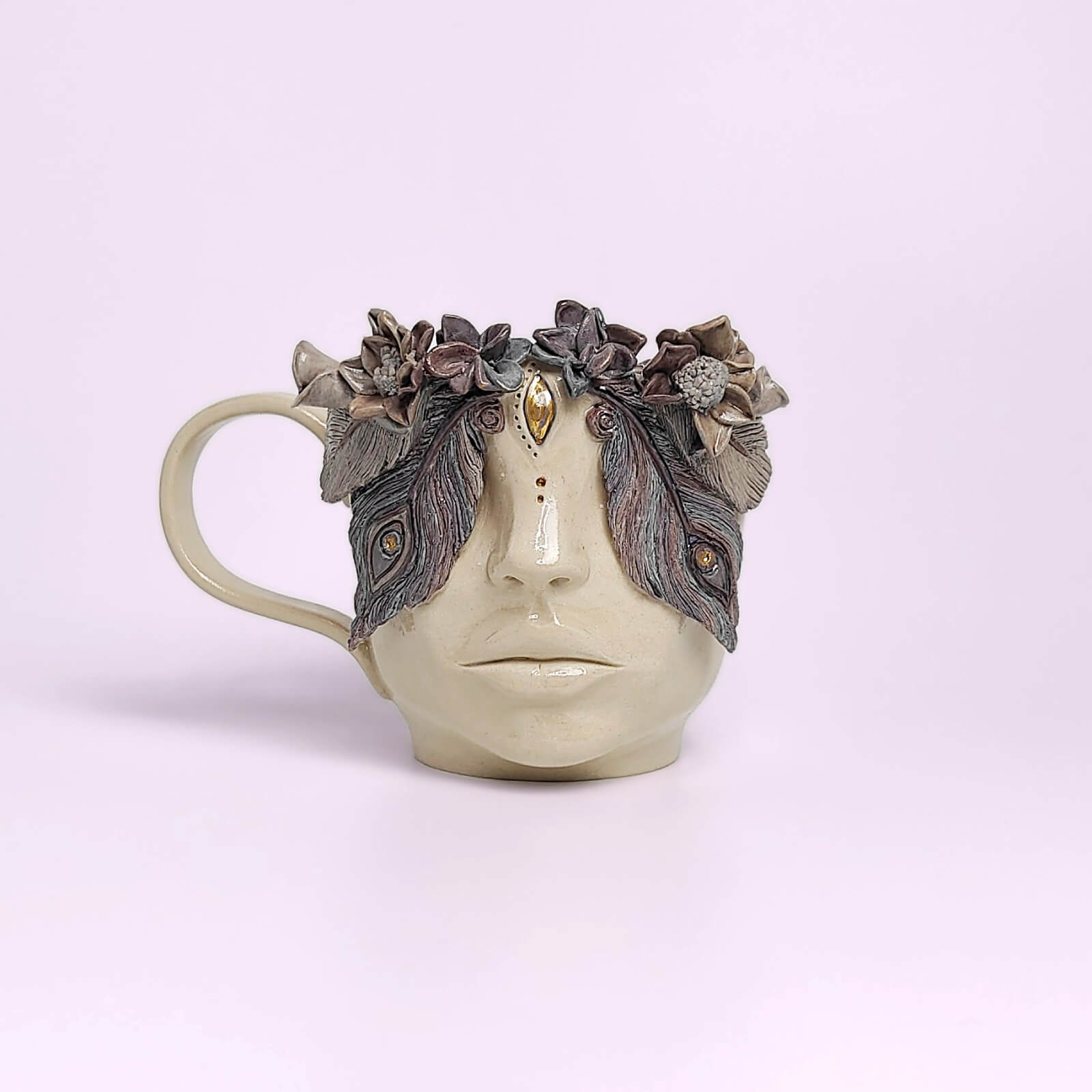 Unique handmade ceramic mug featuring a sculpted human face, textured floral crown, and detailed artistic relief elements