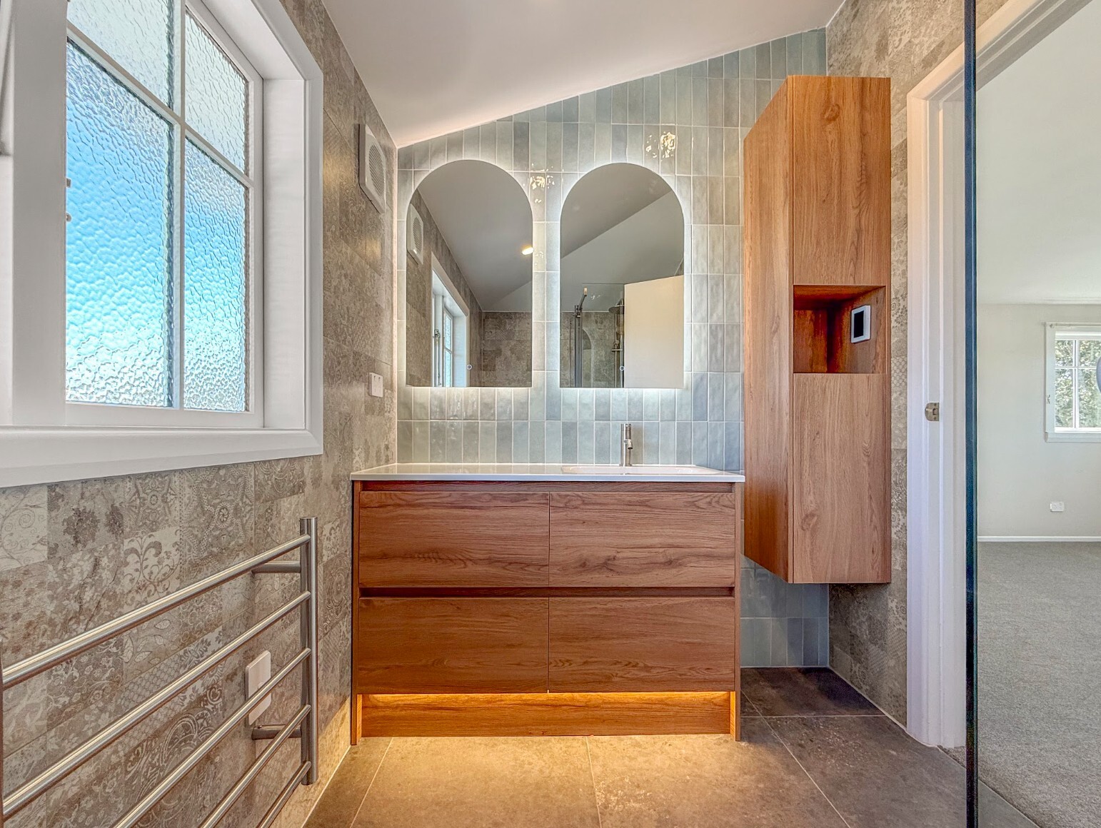 Renovated bathroom vanity with timber cabinetry, twin backlit arched mirrors and pale blue wall tiles