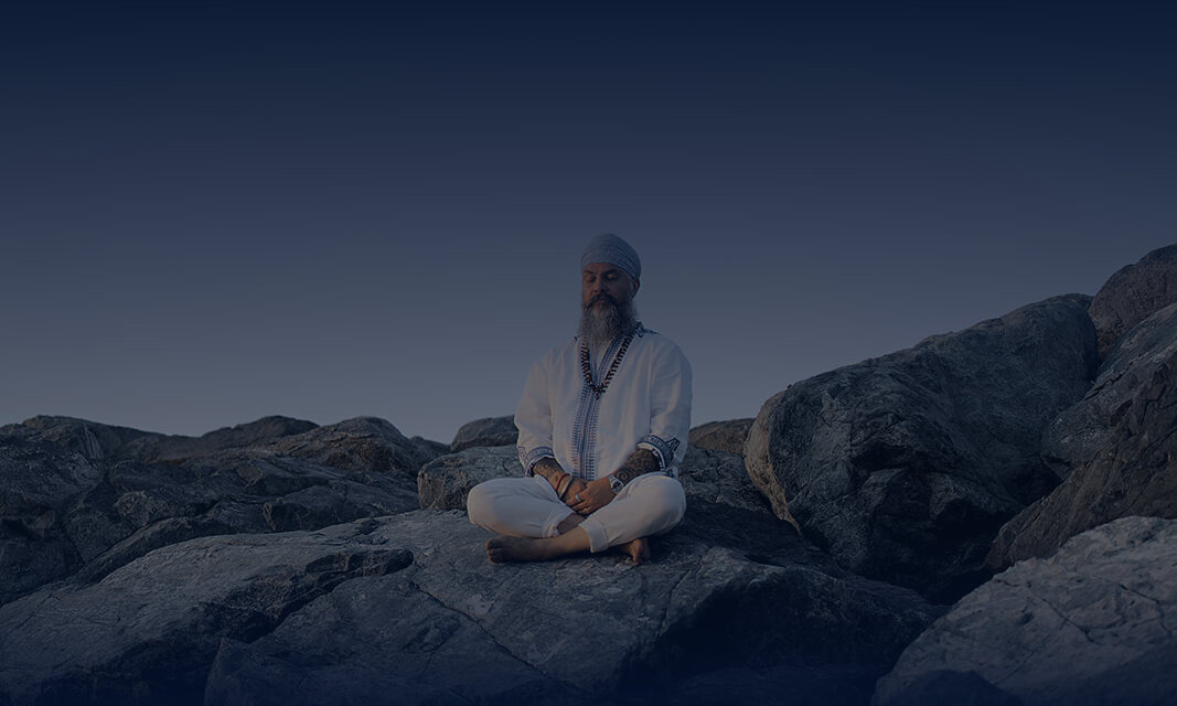 Jugat Guru meditating in white on rocks under a dusk sky