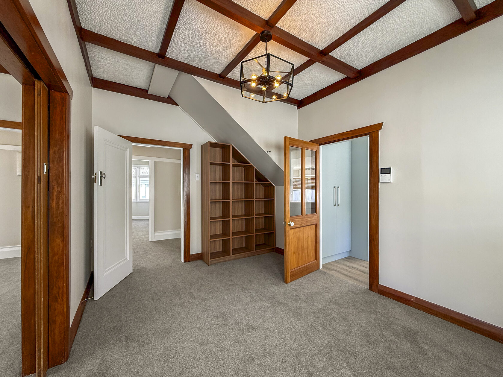 Carpeted interior with dark timber ceiling beams and under-stairs shelving