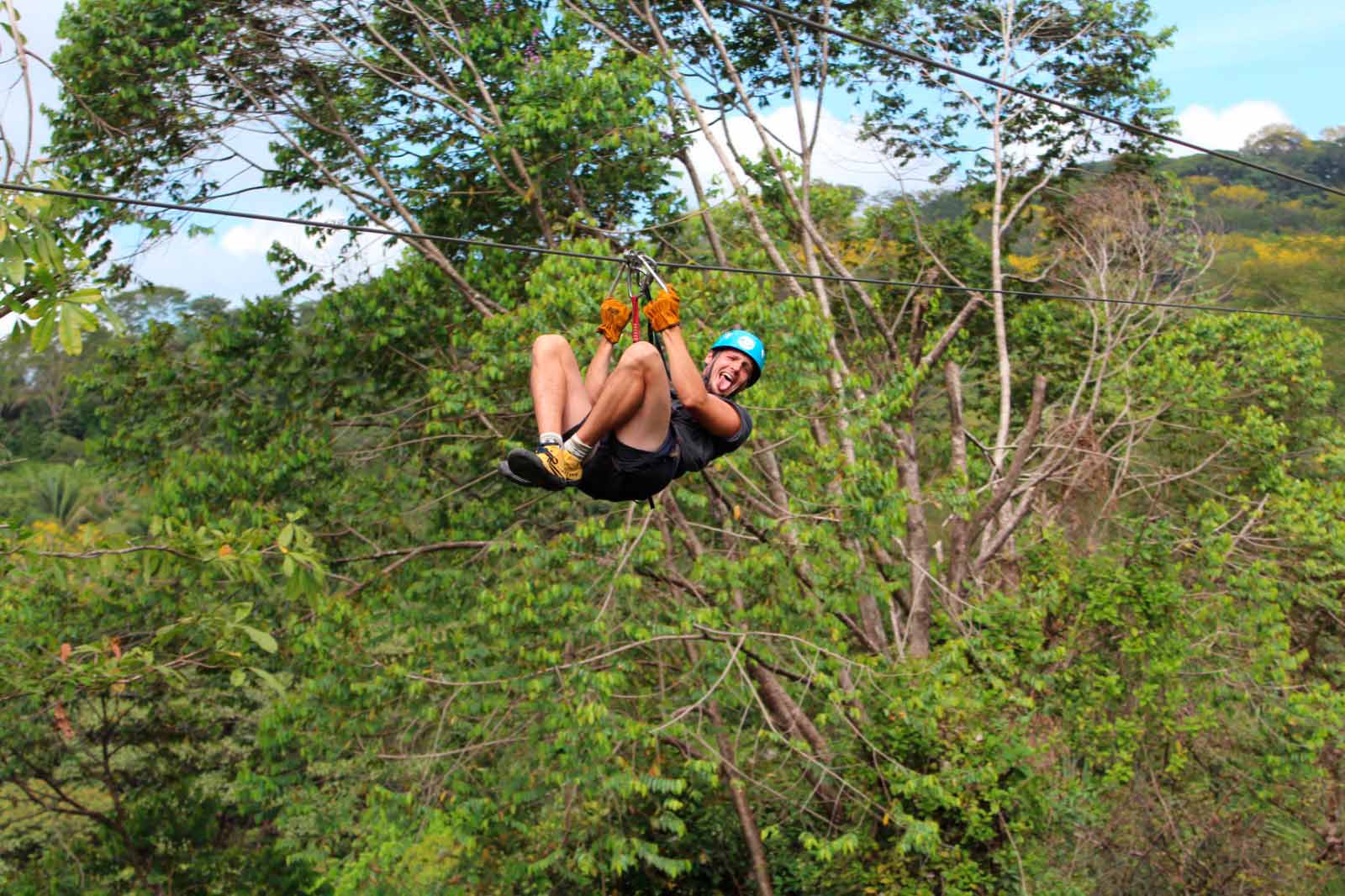 Hombre con casco y guantes deslizándose en zipline boca abajo por el bosque tropical