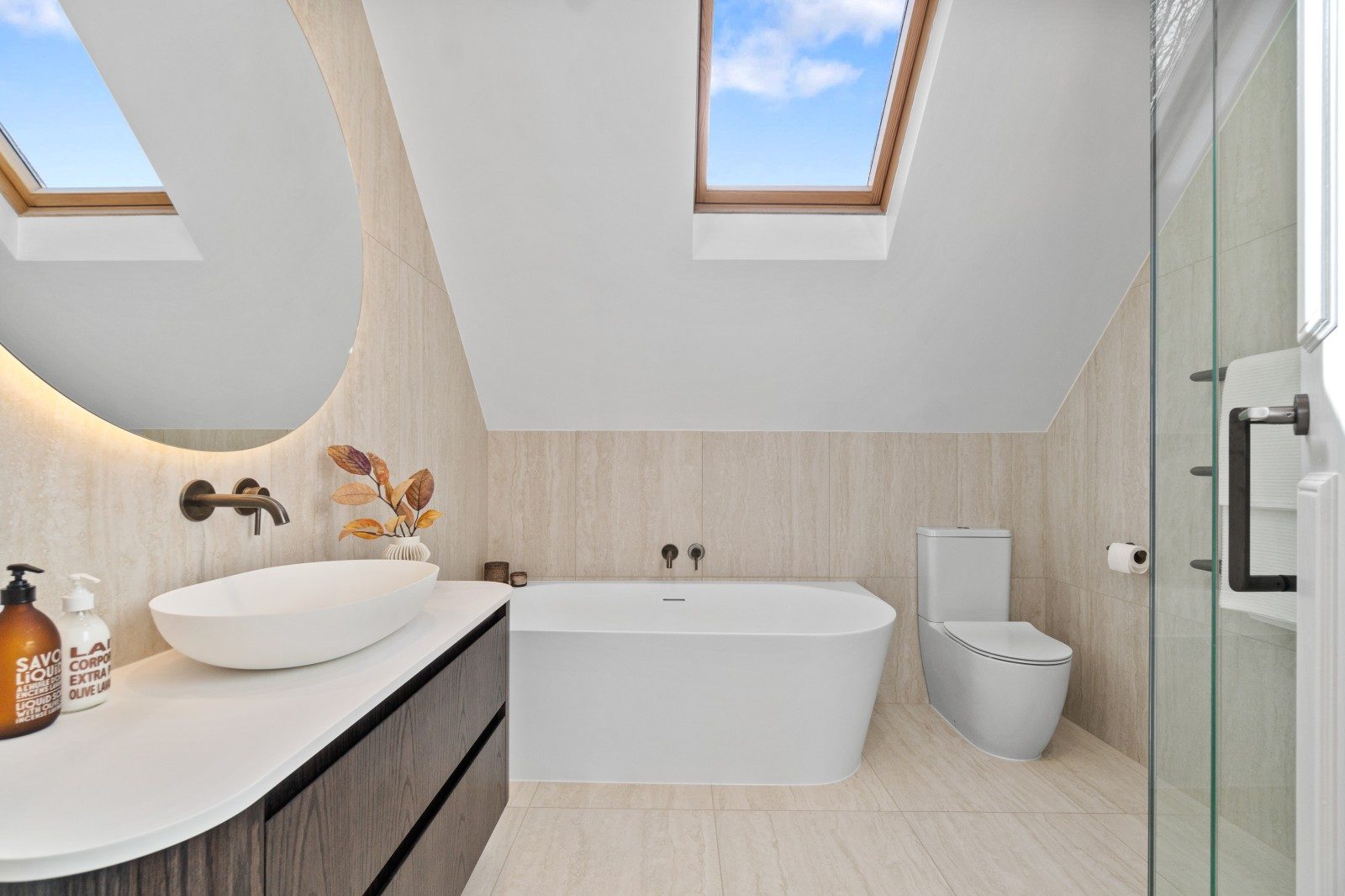 Owens Road bathroom with skylights, an illuminated oval mirror, vanity and glass shower enclosure