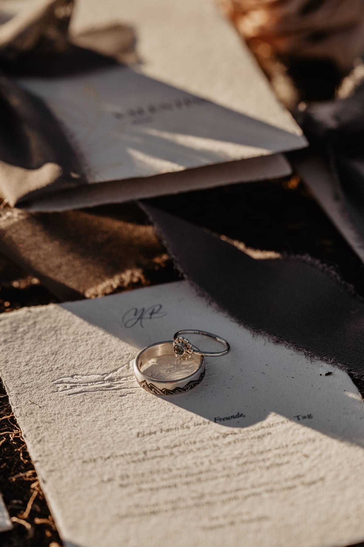 Two wedding rings on textured paper in soft sunlight, with dramatic shadows falling across the wedding details