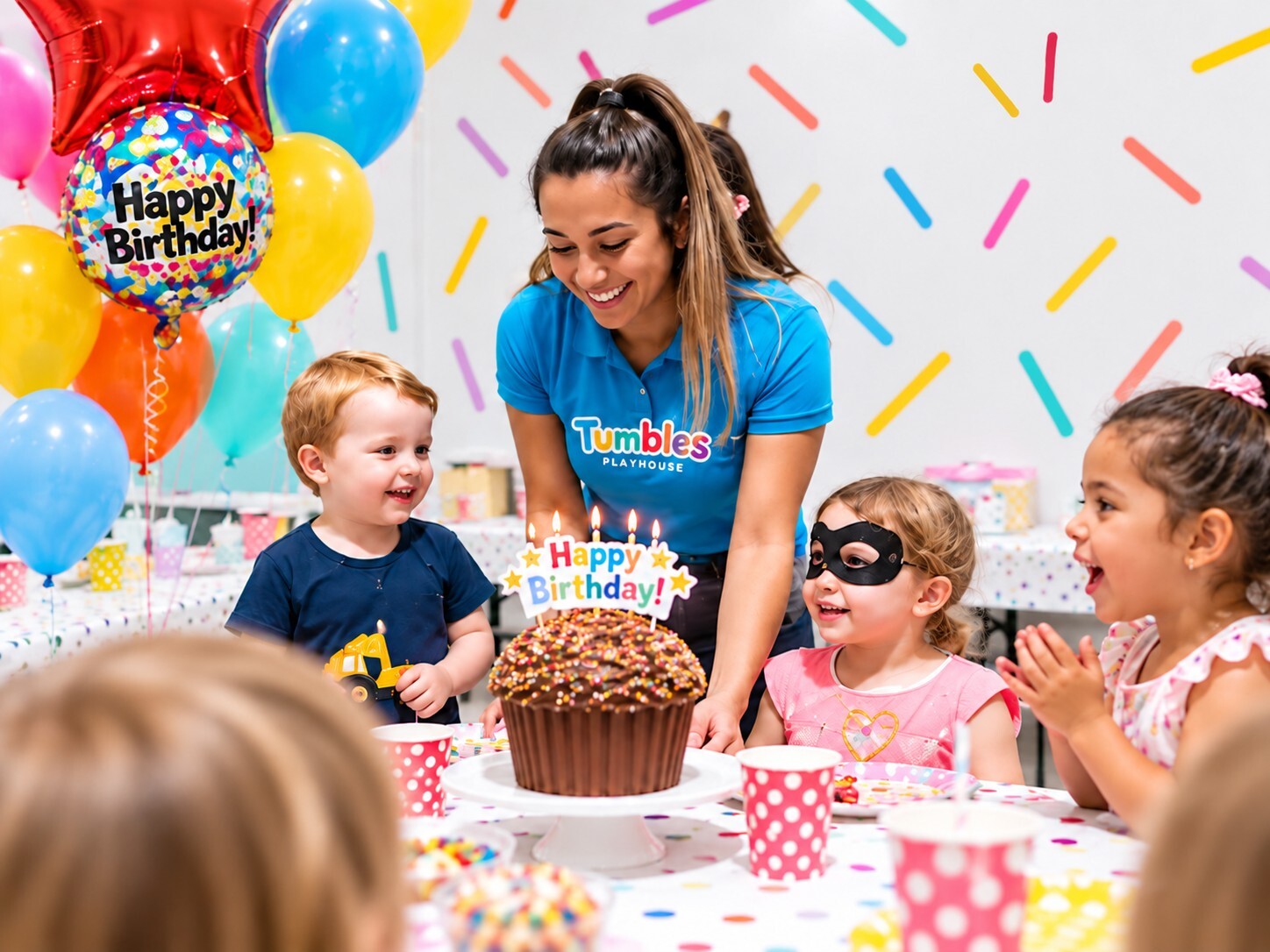 Tumbles themed birthday party with unicorn balloons, a giant purple cupcake cake and children with party hats