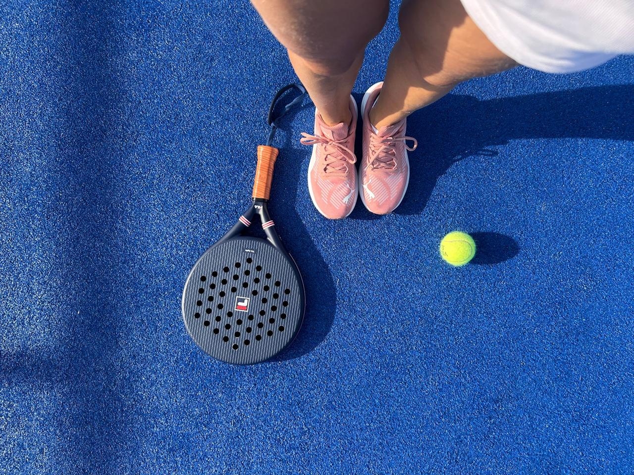 A padel racket and a lime ball on a blue court
