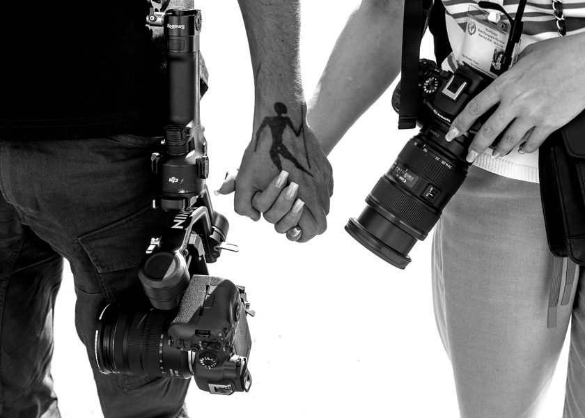 Two photographers holding hands while carrying professional cameras.