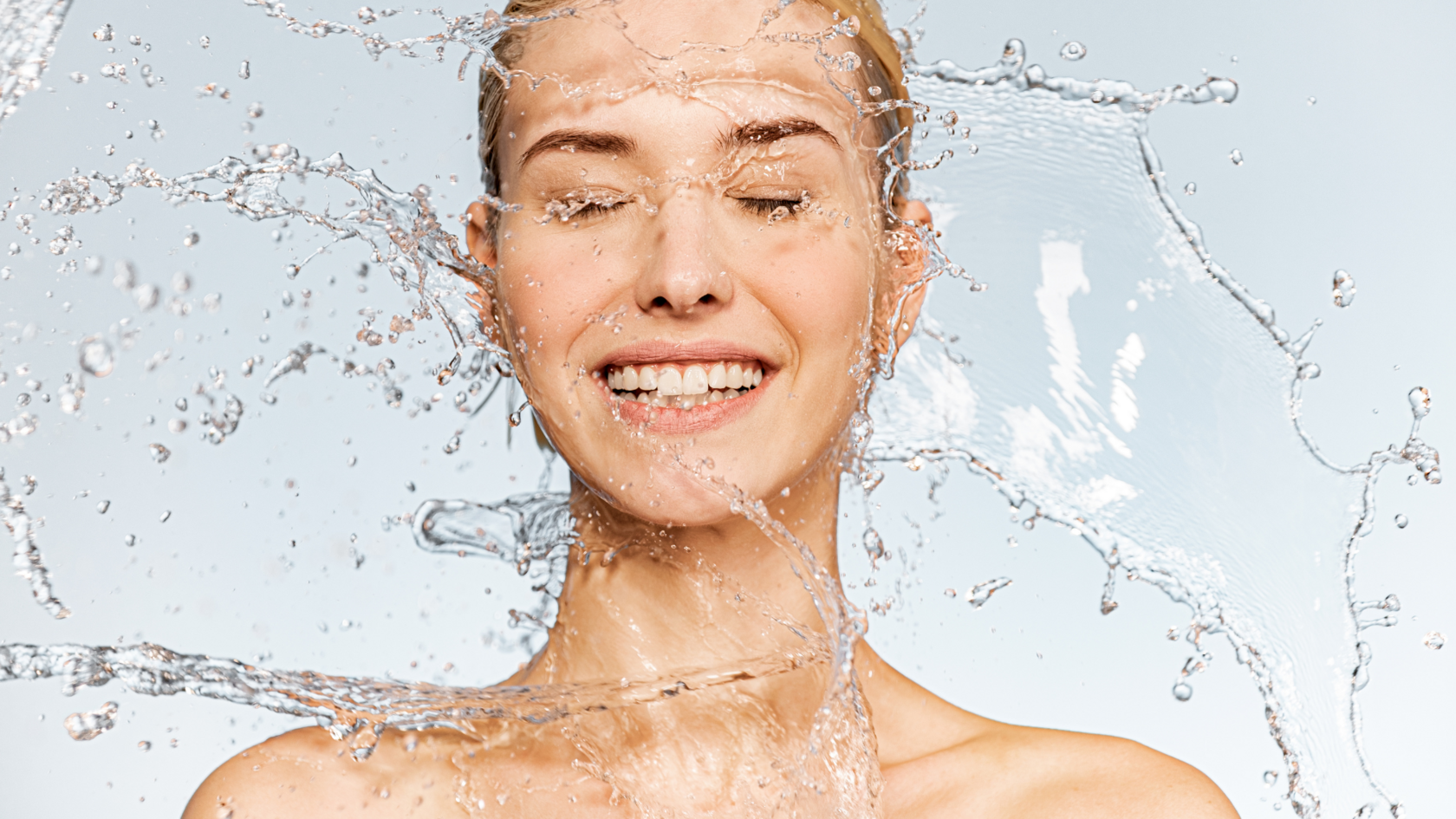 A smiling woman with radiant skin enjoys a splash of water, symbolizing the importance of understanding the benefits and risks of soft and hard water for skin health