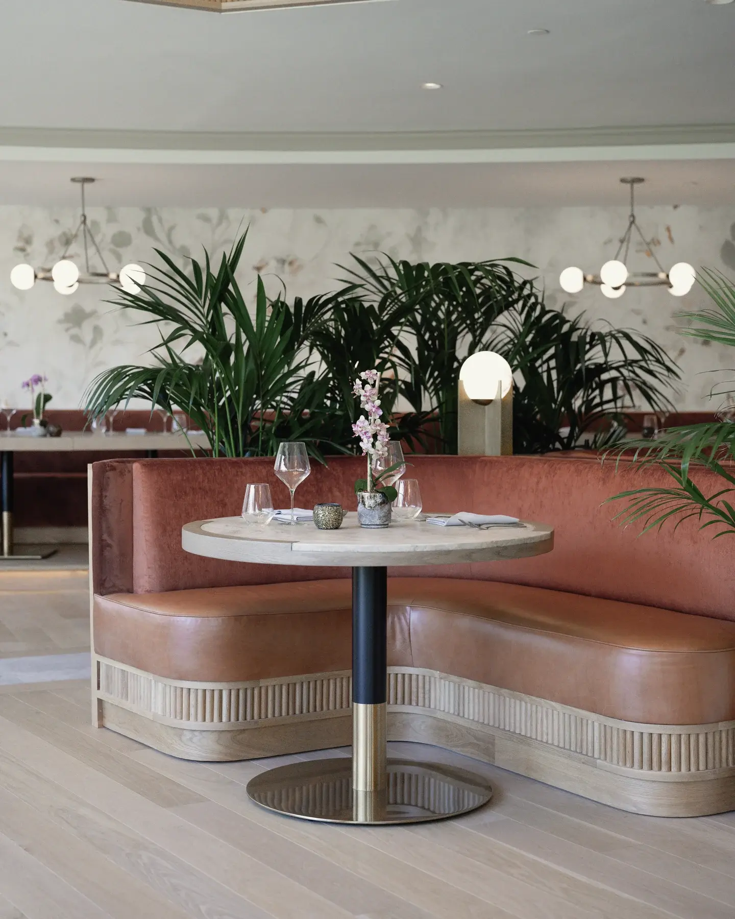 Kentia palms behind a curved dining booth, an orchid on the table, at The Park Club California in Costa Mesa