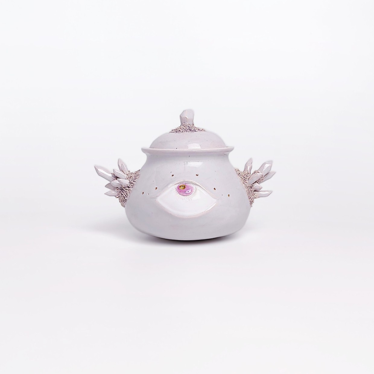 Unique handmade ceramic jar with a sculpted eye, textured crystal-like side elements, and soft pearlescent glaze