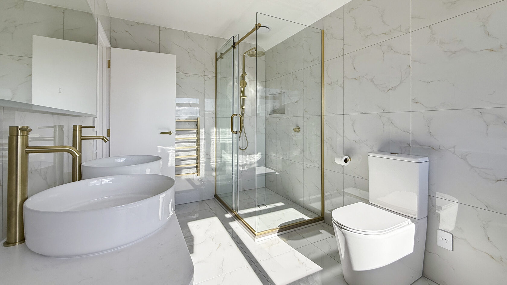 Renovated St Heliers bathroom with double vessel sinks, glass shower and brushed brass fittings.